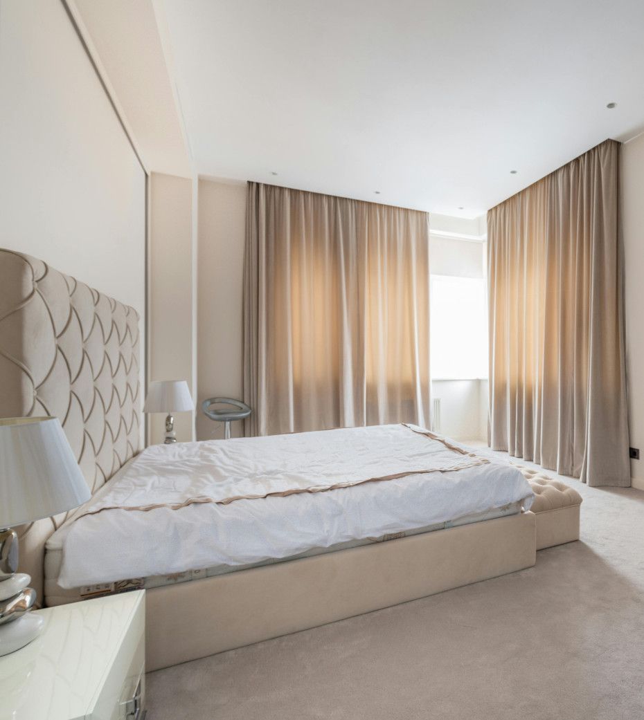 A bedroom with a bed , nightstand , lamp and curtains