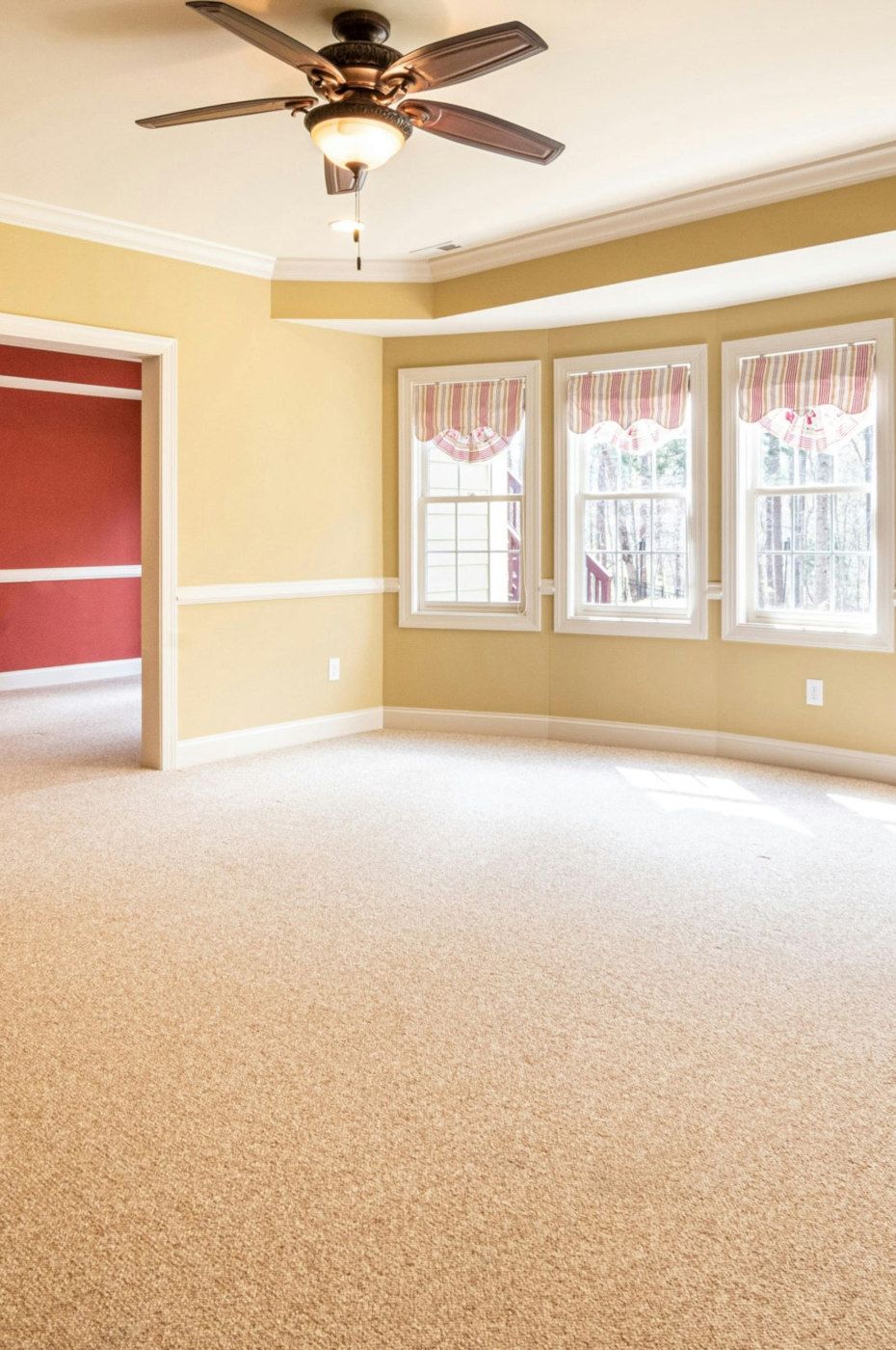 Empty room with beige carpet, yellow walls, and a window bay. A red-walled doorway is visible.