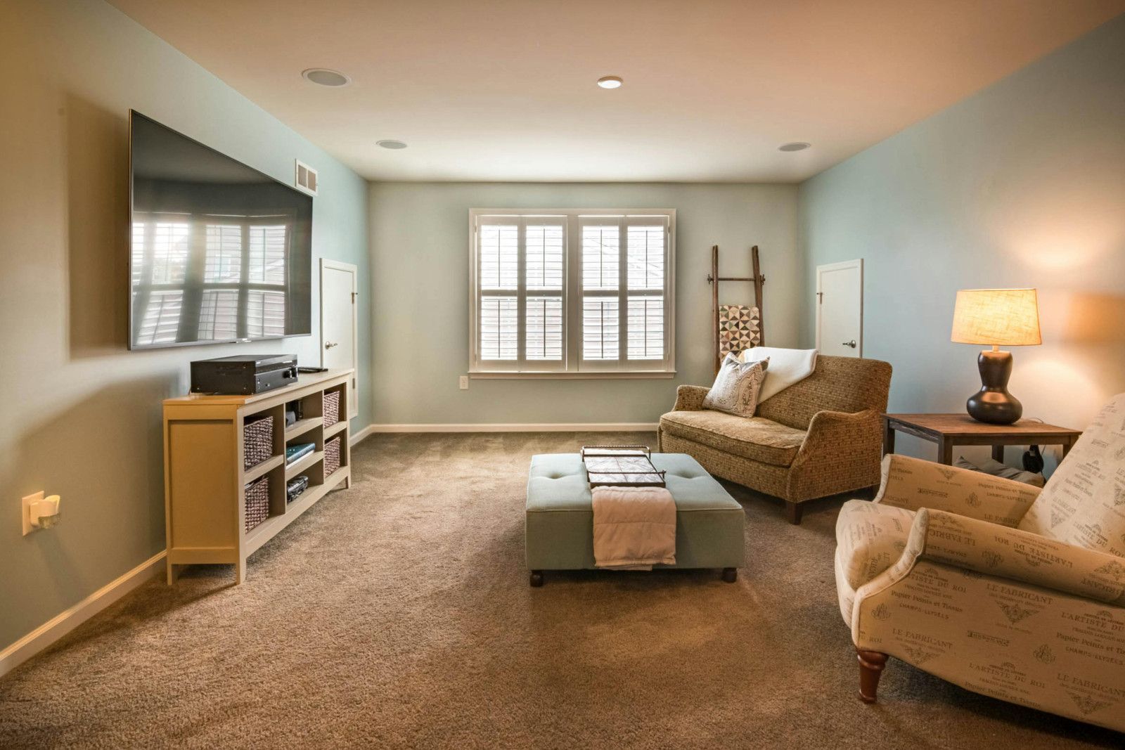 A cozy living room with a TV, couch, armchair, and coffee table, neutral colors, soft carpet, and a window.