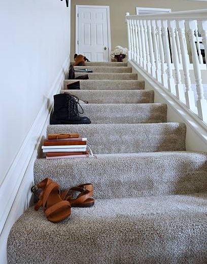 Staircase with assorted shoes and books on the steps; white walls and railing.