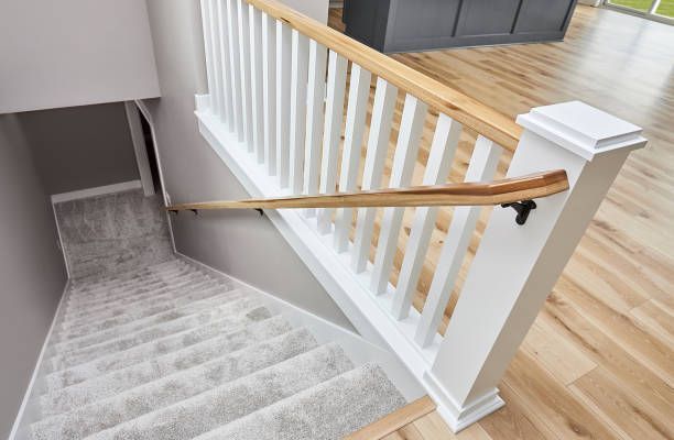 Staircase leading downwards with white railing, wooden handrail, carpeted steps.
