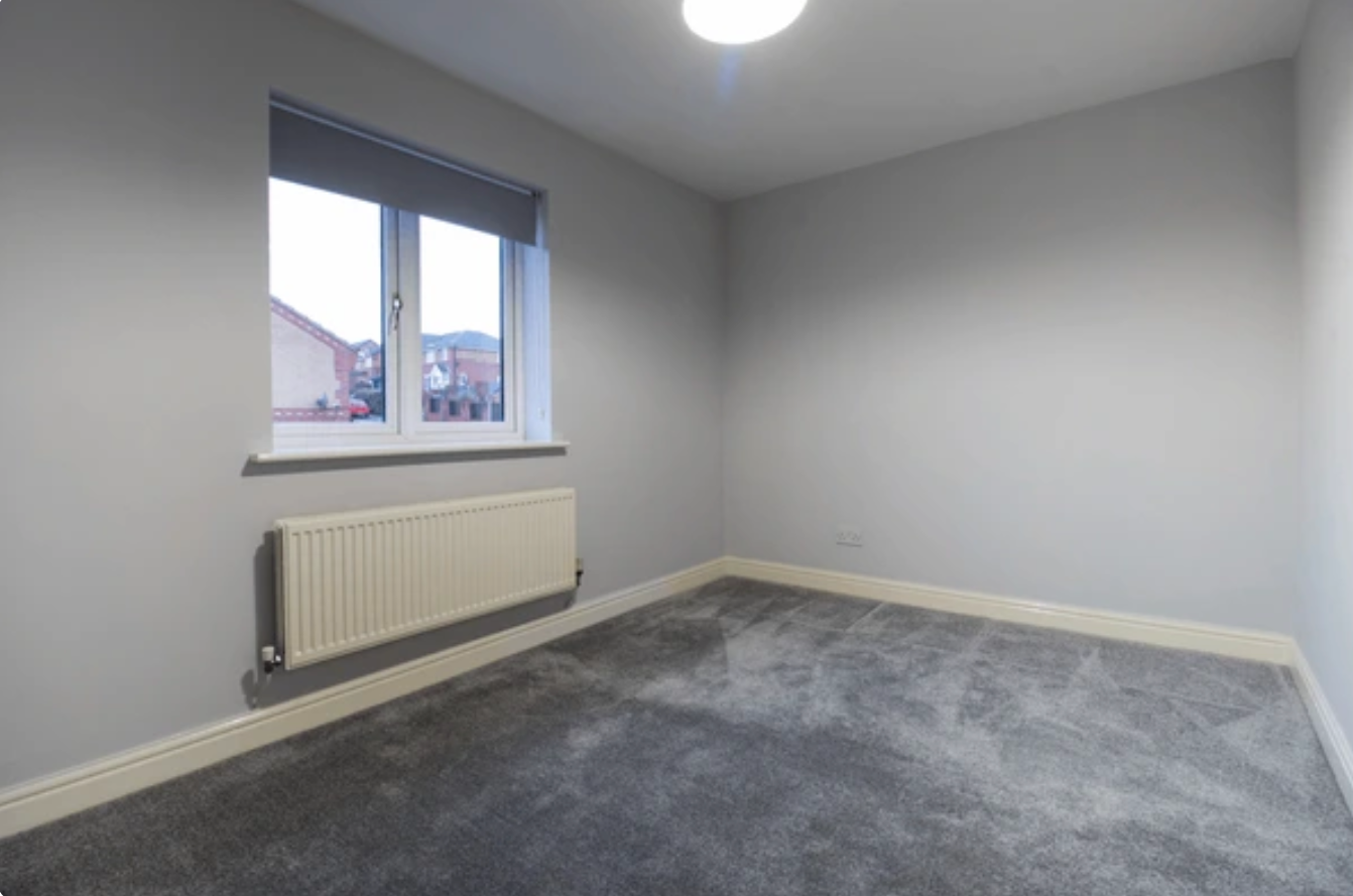Empty bedroom with gray walls, carpet, and a window with a radiator below.