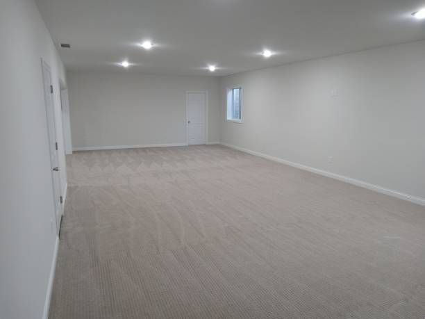 Empty room with neutral carpet and walls, several recessed lights, two doors, and a small window.