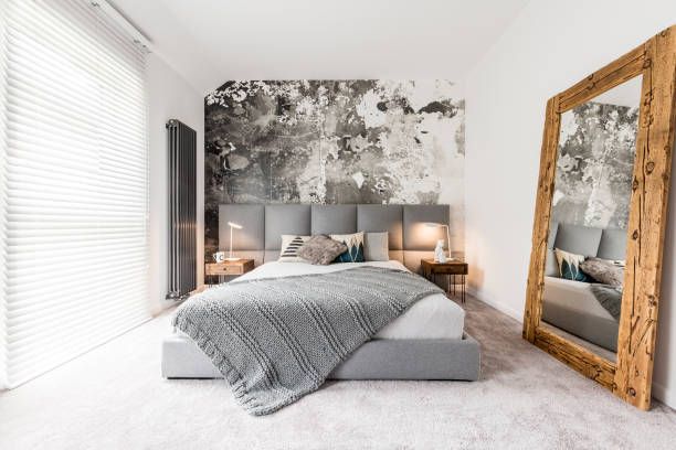 Bedroom with gray and white decor; a distressed wall behind the bed, oversized wooden mirror.