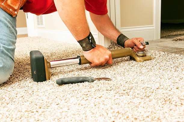 Person installing carpet, using a knee kicker and knife near a doorway.
