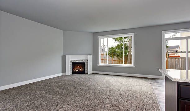 Empty living room with fireplace, windows, and gray carpet.