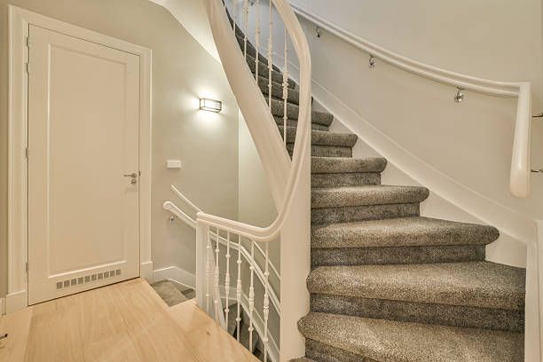 Staircase with carpeted steps and white banister next to a door and wall, light-colored wood floor.