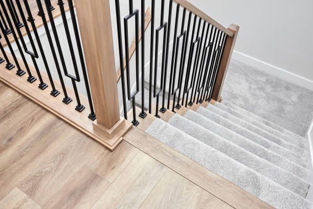 Staircase with wooden handrail, black vertical bars, and carpeted steps.