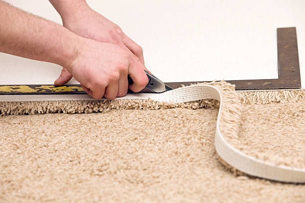 Person using a utility knife to trim carpet along a metal square, close-up shot.
