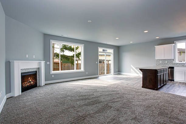 Spacious living room with gray walls, carpet, fireplace, and kitchen island; large windows provide natural light.