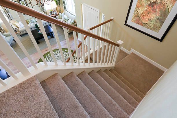 Staircase with beige carpet, white balusters, and wooden handrail. Leads down to a living room.
