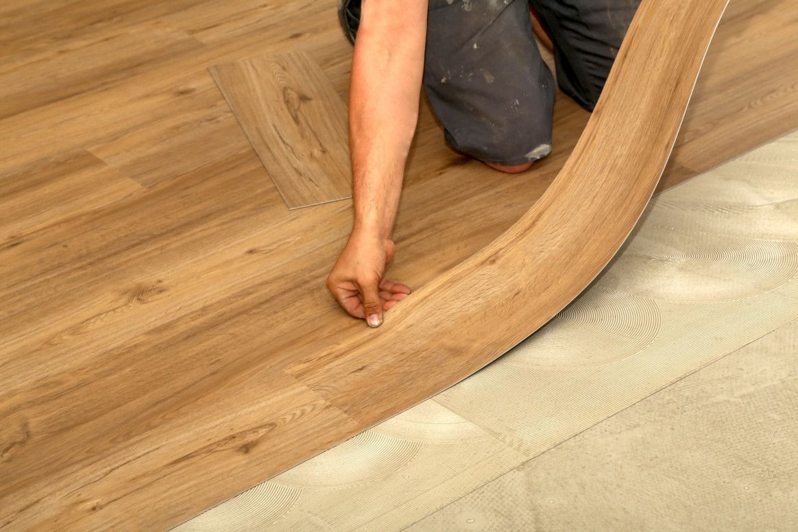 Person installing wood flooring, bending a plank into place.