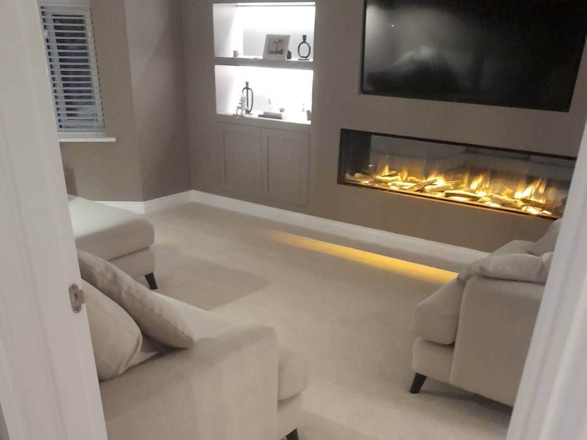 Cozy living room with electric fireplace, built-in shelves, TV, two beige armchairs, and beige carpet.