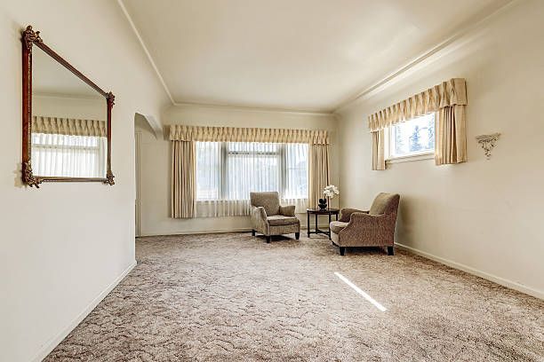 Empty living room with beige carpet, white walls, two armchairs, and a mirror.