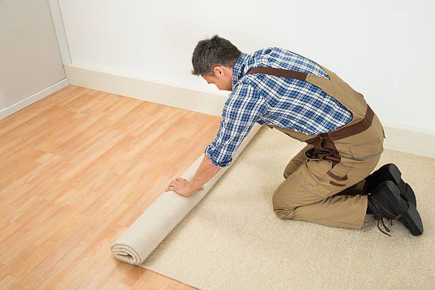 Male worker unrolling carpet on floor at home