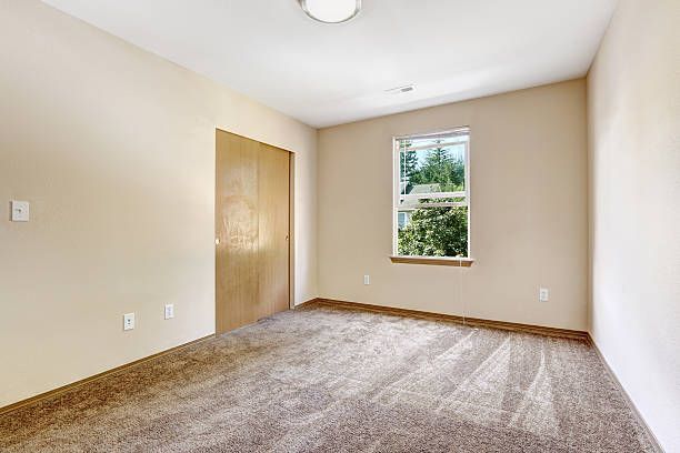 Empty room with tan walls, wood closet, small window, and brown carpet.