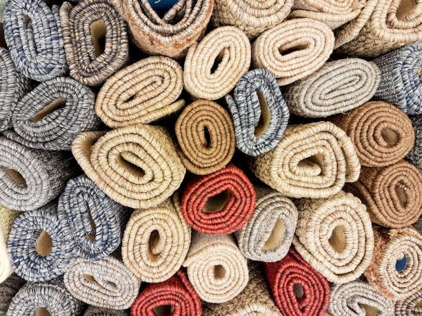 Rolled rugs in various colors: beige, brown, red, and blue, stacked together.