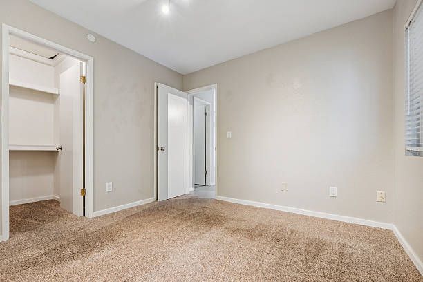 Empty bedroom with cream-colored walls and carpet, large windows, and an open closet.
