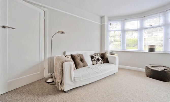 White sofa in a light-filled living room with bay windows and a floor lamp.