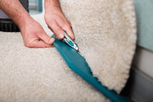 Person trimming carpet edge with a utility knife and blue guide.