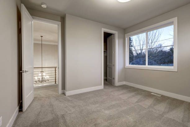 Empty room with gray carpet, walls, and doors. A window offers an outside view.
