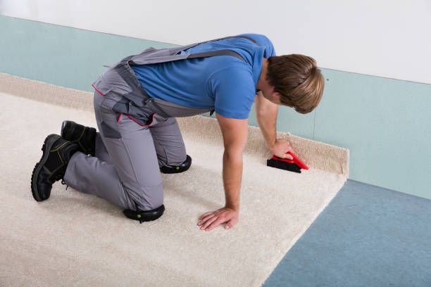Young male craftsman fitting carpet on floor