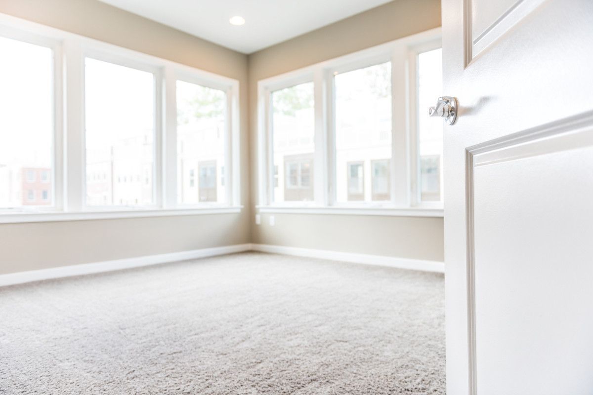 Empty room with large windows, light carpet, and partially open white door.