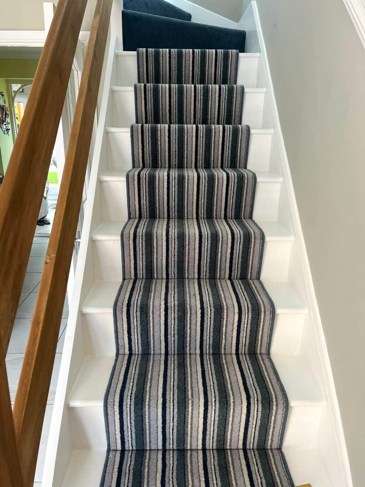 Staircase with white risers and patterned carpet runner in shades of blue, gray, and white.