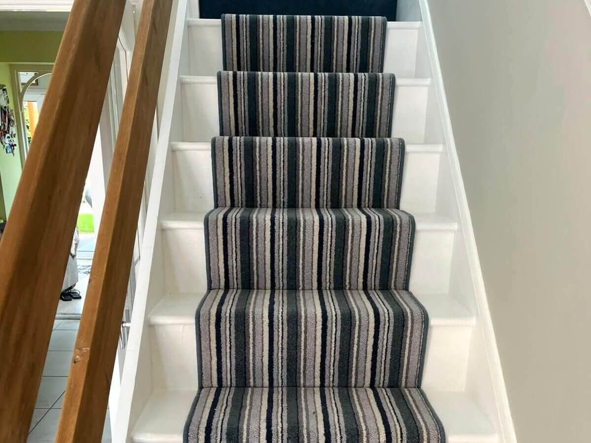 Staircase with white risers and patterned carpet runner in shades of black, gray, and beige.