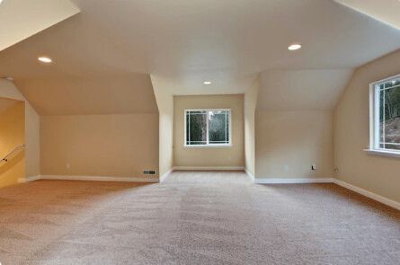 Empty room with beige walls, carpet, and two windows; recessed lighting.