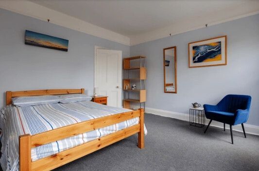 Bedroom with blue walls, wooden bed, blue chair, and art.