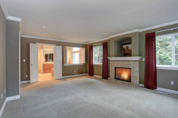 Empty master bedroom with fireplace, windows, and burgundy curtains.