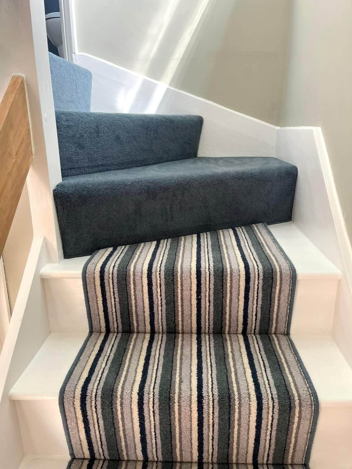 Staircase with striped carpet runner and gray carpet on the steps. White painted risers and side panels.