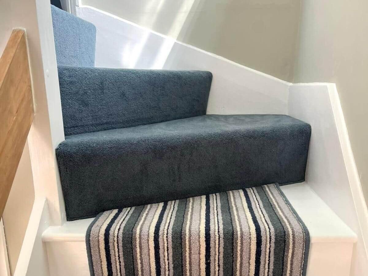 Carpeted stairs with dark blue steps and a striped runner on white risers.