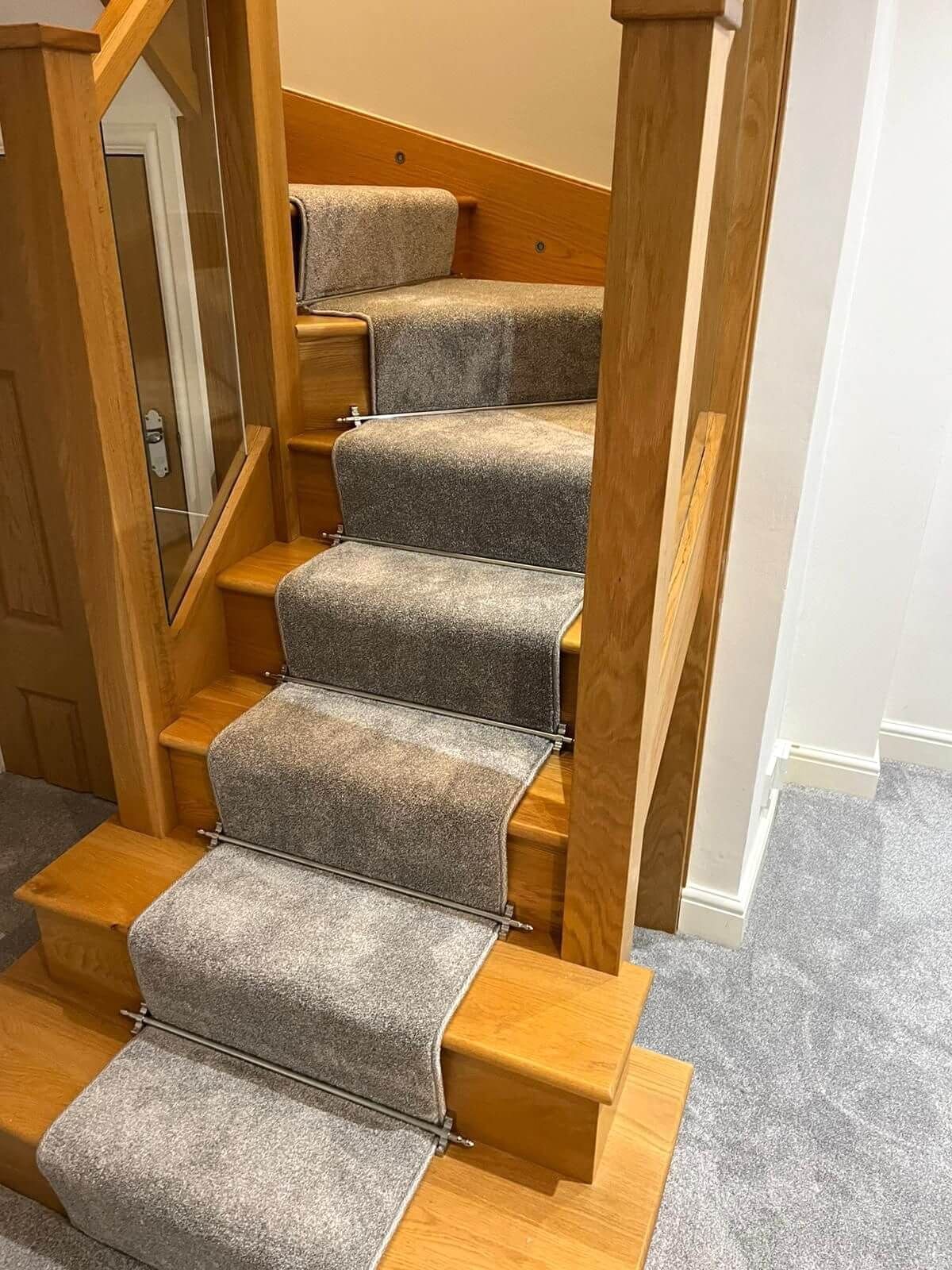 Staircase with gray carpet runner, light wood treads and railings. Glass panel and white wall on sides.