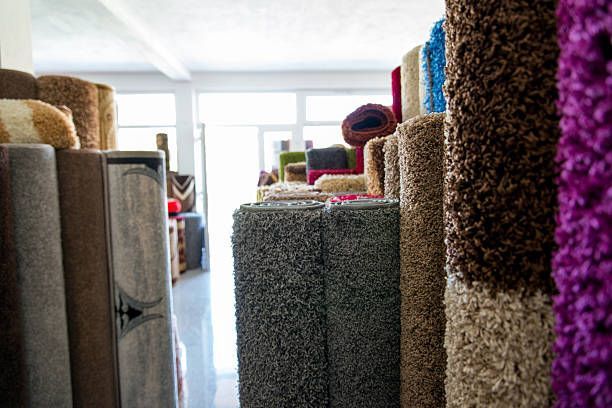 Rolled carpets in various colors displayed in a store, with a bright interior and natural light.