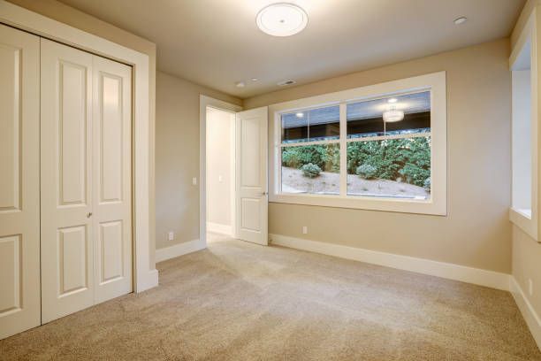 Empty room with tan walls, carpet, and white trim; closet doors on the left, a window, and open doorway.