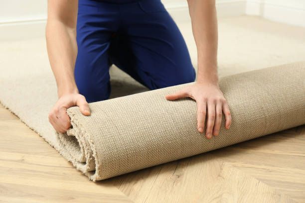Person rolling up a beige rug on a wooden floor.