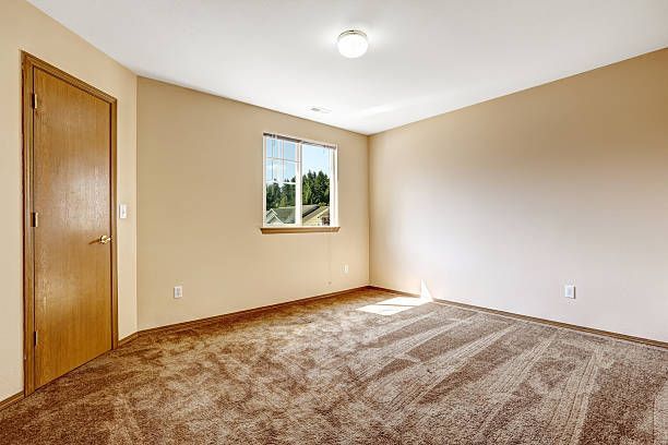 Empty bedroom with beige walls, brown carpet, and a wooden door.