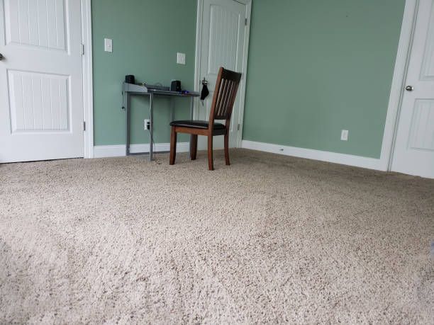 A room with beige carpet, green walls, and a brown chair; a desk with items sits in the corner.