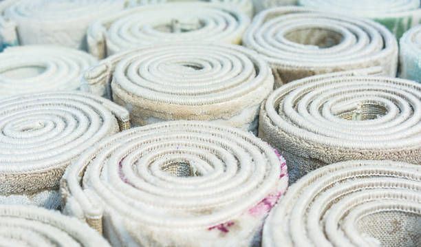 Rolled-up carpets of varying sizes, with beige and white tones, stacked closely together.