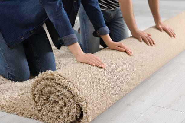 Two people unrolling a beige carpet on a light wooden floor.
