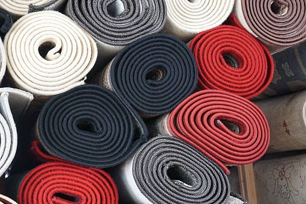 Rolled carpets, varying colors: white, gray, black, and red, stacked together.