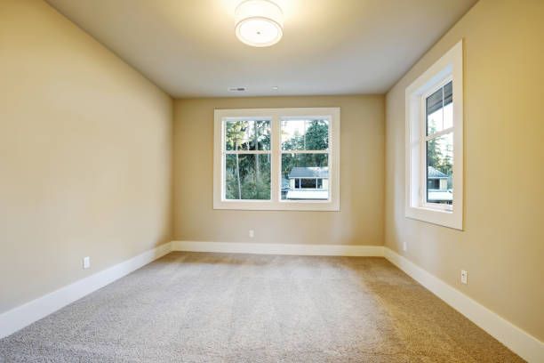 Empty room with beige walls, carpet, two windows, and a ceiling light.