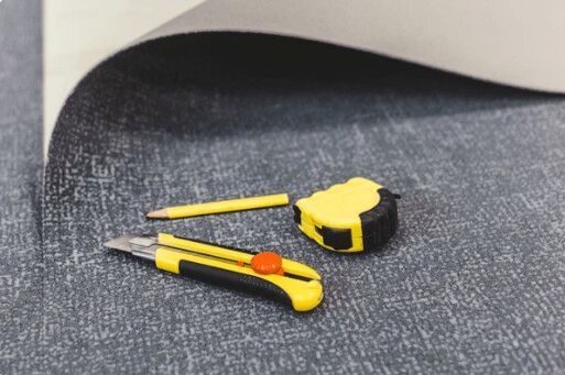 Gray patterned surface with a yellow utility knife, pencil, and measuring tape. A corner of paper is flipped up.