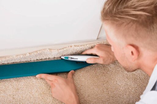 Man trimming carpet along a wall edge with a blue trimming tool.