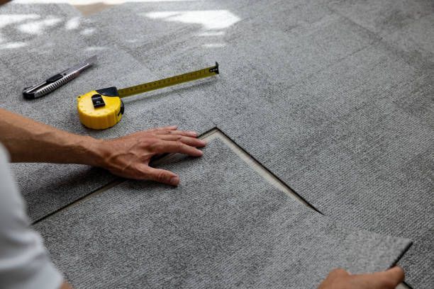 Person cutting and placing gray tile with a tape measure and utility knife on a floor.