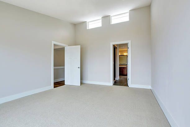 Empty bedroom with light-colored walls, carpet, and two doorways leading to other rooms.