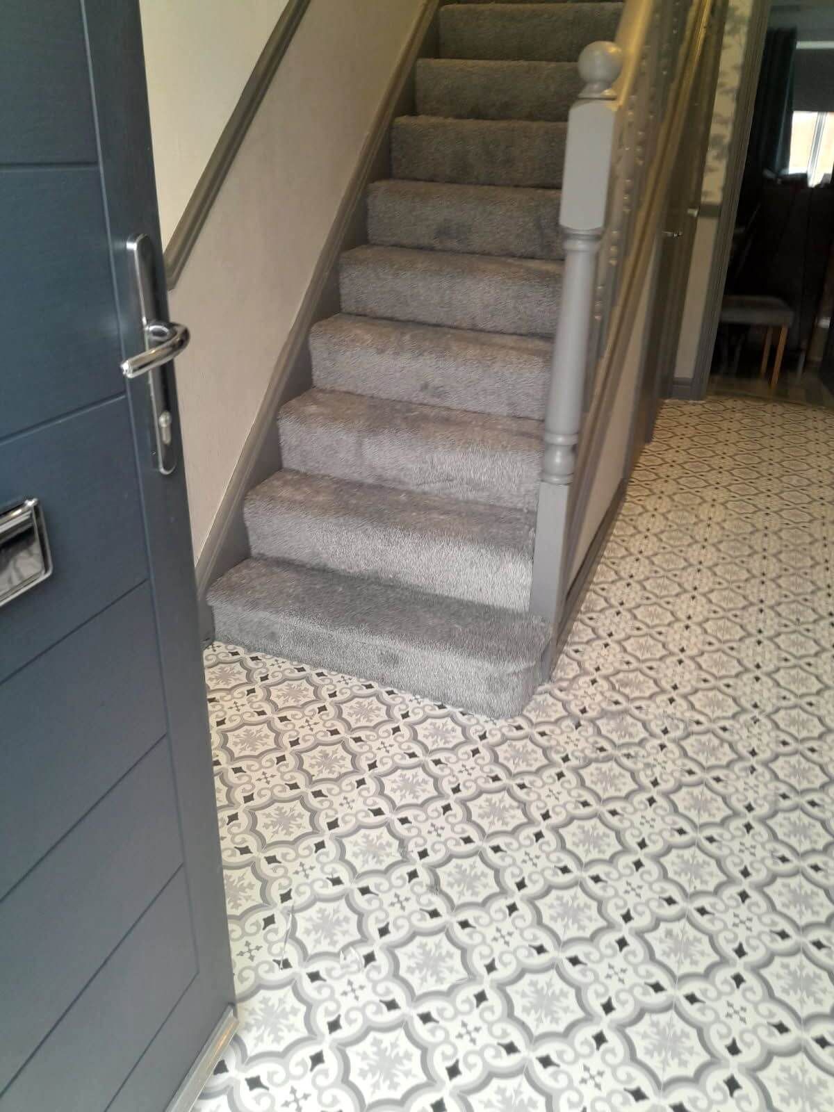 Entryway with patterned tile floor, carpeted stairs, gray banister, and blue front door.
