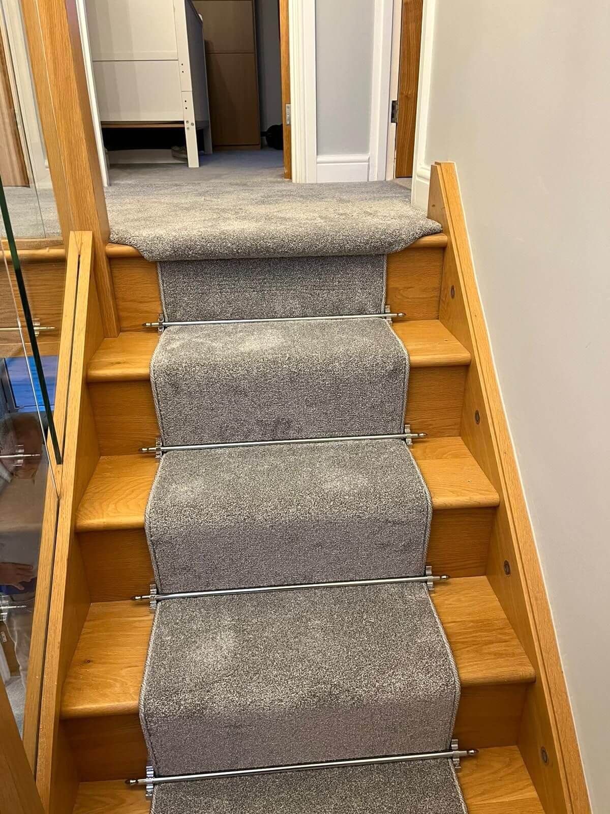 Carpeted wooden staircase with gray carpet runner and metal rods.